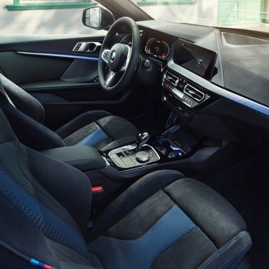 Interior desportivo do BMW Série 1. Posto de condução do BMW Série 1 com bancos desportivos M, volante M em pele e frisos interiores iluminados.
