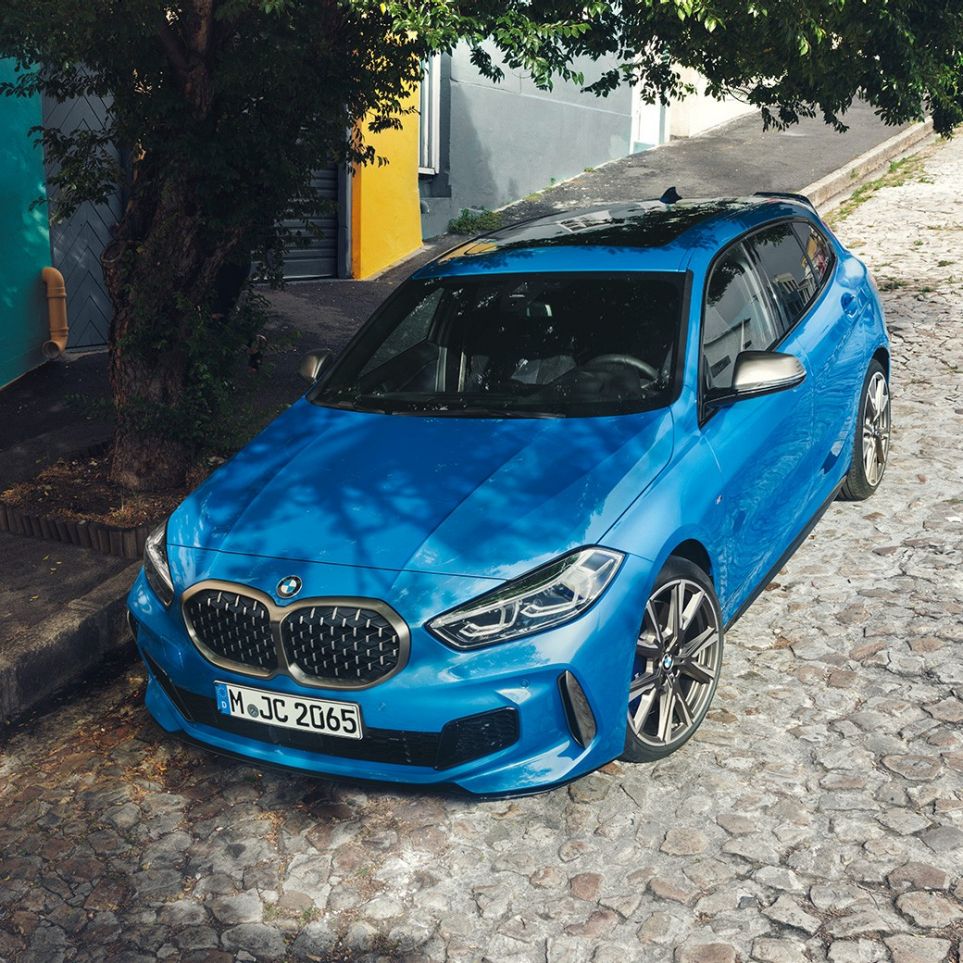 BMW Série 1 na berma da estrada. BMW Série 1 na pintura azul Misano metalizada a estacionar na berma da estrada, perspetiva frontal de topo a três quartos.