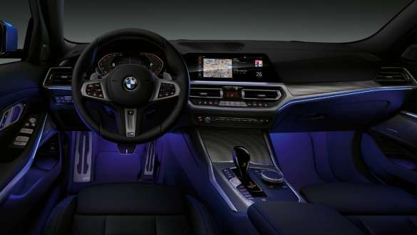 BMW Série 3 Berlina, luz ambiente. Perspetiva frontal do interior do BMW Série 3 Berlina com o espaço para as pernas iluminado a azul pela luz ambiente.