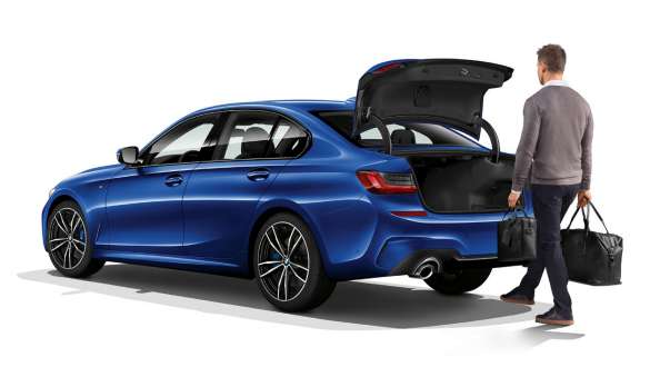BMW Série 3 Berlina (G20), funcionamento automático da bagageira. Perspetiva traseira a três quartos do BMW Série 3 Berlina (G20) parado e o condutor a abrir automaticamente a porta da bagageira com o pé.