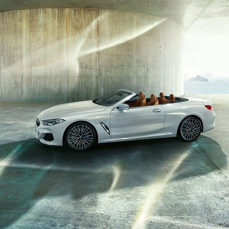 BMW M850i xDrive em branco Mineral metalizado, perspetiva lateral com capota flexível aberta. BMW M850i xDrive em branco Mineral metalizado, perspetiva lateral com capota flexível aberta.