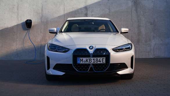 Perspetiva frontal com uma BMW Wallbox, BMW i4 eDrive40, G26, 2021 BMW i4 eDrive40, G26, 2021, pintura branco Mineral metalizada, perspetiva frontal, em frente a uma parede de uma casa com uma BMW Wallbox, posto de carregamento