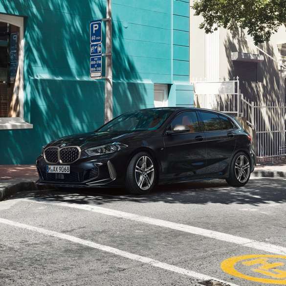 BMW M135i xDrive, perspetiva lateral a três quartos. Novo BMW M135i xDrive na pintura preto Sapphire metalizada, a estacionar, perspetiva lateral a três quartos.