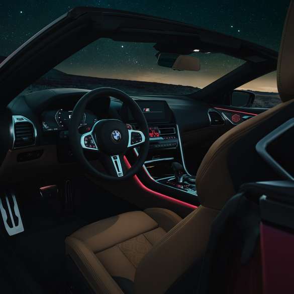 BMW M8 Competition Cabrio, posto de condução. BMW M8 Competition Cabrio, posto de condução à noite, com volante M em pele e luz ambiente em vermelho.
