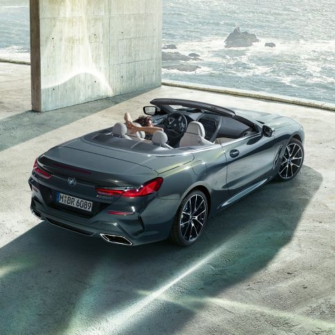 BMW M850i xDrive Cabrio, perspetiva aérea. BMW M850i xDrive Cabrio na pintura cinza Dravit metalizada com capota flexível aberta, estacionado no interior de um edifício em betão, em frente ao mar, perspetiva aérea.