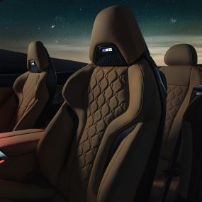 Bancos desportivos M em pele Merino. BMW M8 Competition Cabrio com capota flexível aberta sob um céu estrelado, interior com bancos desportivos M em pele Merino e luz ambiente em vermelho.