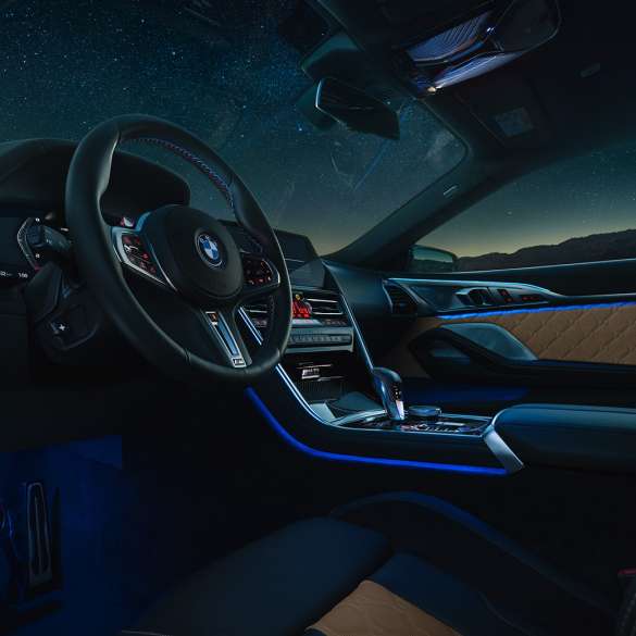 BMW M8 Competition Coupé, posto de condução. BMW M8 Competition Coupé, posto de condução à noite, com volante M em pele e luz ambiente em azul.