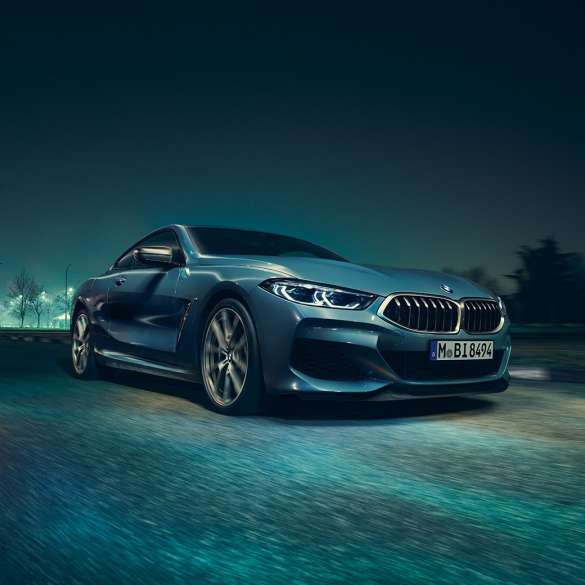 BMW M850i xDrive Coupé, perspetiva frontal esquerda a três quartos. BMW M850i xDrive Coupé na pintura azul Barcelona metalizada, em movimento à noite, perspetiva frontal esquerda a três quartos.