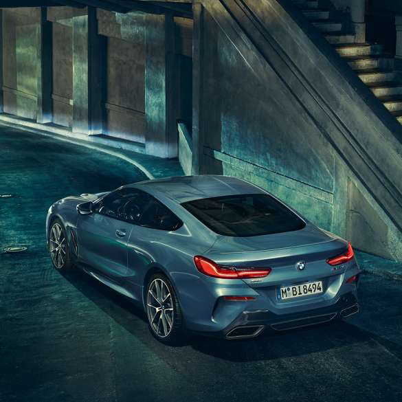 BMW M850i xDrive Coupé, perspetiva traseira esquerda a três quartos. BMW M850i xDrive Coupé na pintura azul Barcelona metalizada, parado à noite, perspetiva traseira esquerda a três quartos.
