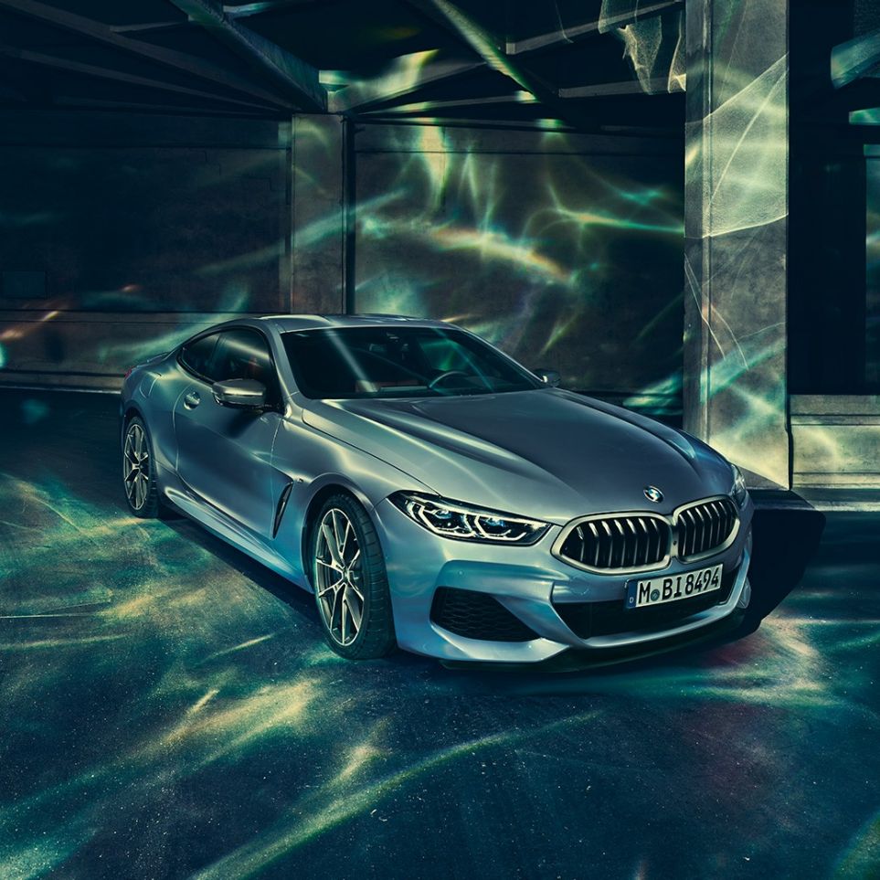 BMW M850i xDrive Coupé, perspetiva frontal esquerda a três quartos. BMW M850i xDrive Coupé na pintura azul Barcelona metalizada, parado em frente a um edifício, perspetiva frontal esquerda a três quartos.