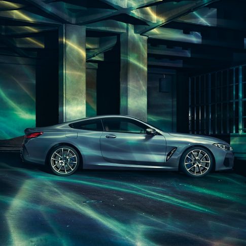 BMW M850i xDrive Coupé, perspetiva lateral. BMW M850i xDrive Coupé na pintura azul Barcelona metalizada, parado em frente a um edifício, perspetiva lateral.