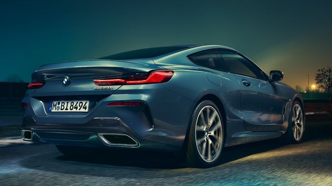 BMW M850i xDrive Coupé, perspetiva traseira. BMW M850i xDrive Coupé na pintura azul Barcelona metalizada, em movimento à noite, perspetiva traseira.