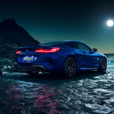 BMW M8 Competition Coupé, perspetiva traseira a três quartos. BMW M8 Competition Coupé na pintura azul Marina Bay metalizada com faróis traseiros LED iluminados, parado num cenário de lua cheia, perspetiva traseira a três quartos.