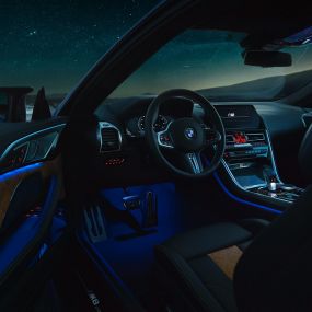 Interior do BMW M8 Competition Coupé. BMW M8 Competition Coupé, interior à noite, com volante M em pele e luz ambiente em azul, com a porta do condutor aberta.