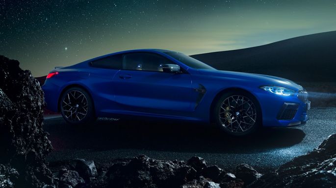 BMW M8 Competition Coupé, perspetiva lateral a três quartos. BMW M8 Competition Coupé na pintura azul Marina Bay metalizada, parado à noite, perspetiva lateral a três quartos.