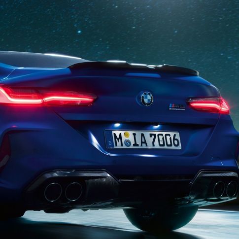 Difusor M em preto Carbon. BMW M8 Competition Coupé na pintura azul Marina Bay metalizada, grande plano da traseira, com o difusor M em preto Carbon à noite.