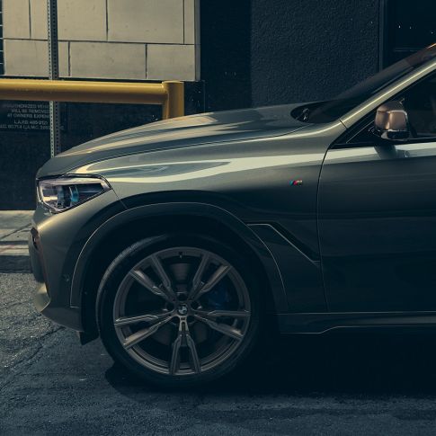 BMW X6 M50i, perspetiva lateral Homem junto ao BMW X6 M50i, perspetiva lateral, em frente a um cenário urbano