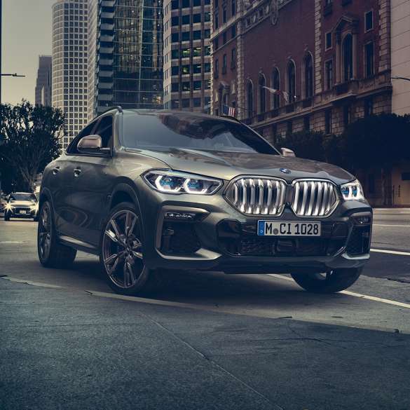 Suspensão adaptativa M Professional do BMW X6 Perspetiva dianteira a três quartos do BMW X6 em frente a um cenário urbano.