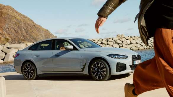 BMW Service Inclusive para veículos novos BMW Service Inclusive, mulher a caminhar em frente a um BMW i4 à beira-mar