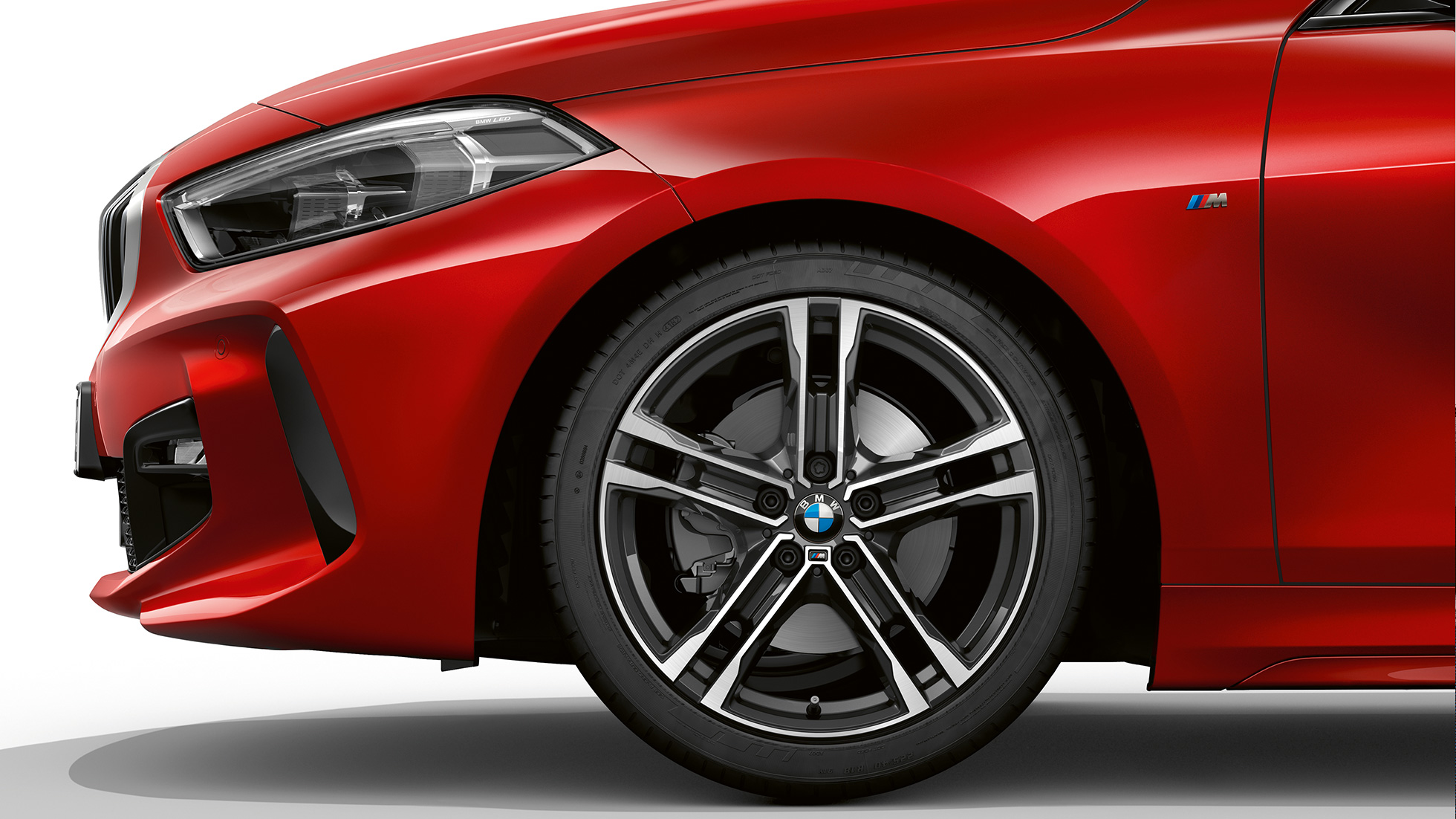 BMW Série 1 Versão Desportiva M, perspetiva frontal lateral. BMW Série 1 na pintura vermelho Melbourne metalizada, Versão Desportiva M, perspetiva frontal lateral das jantes de liga leve BMW 550 M de raios duplos de 17" de duas tonalidades.