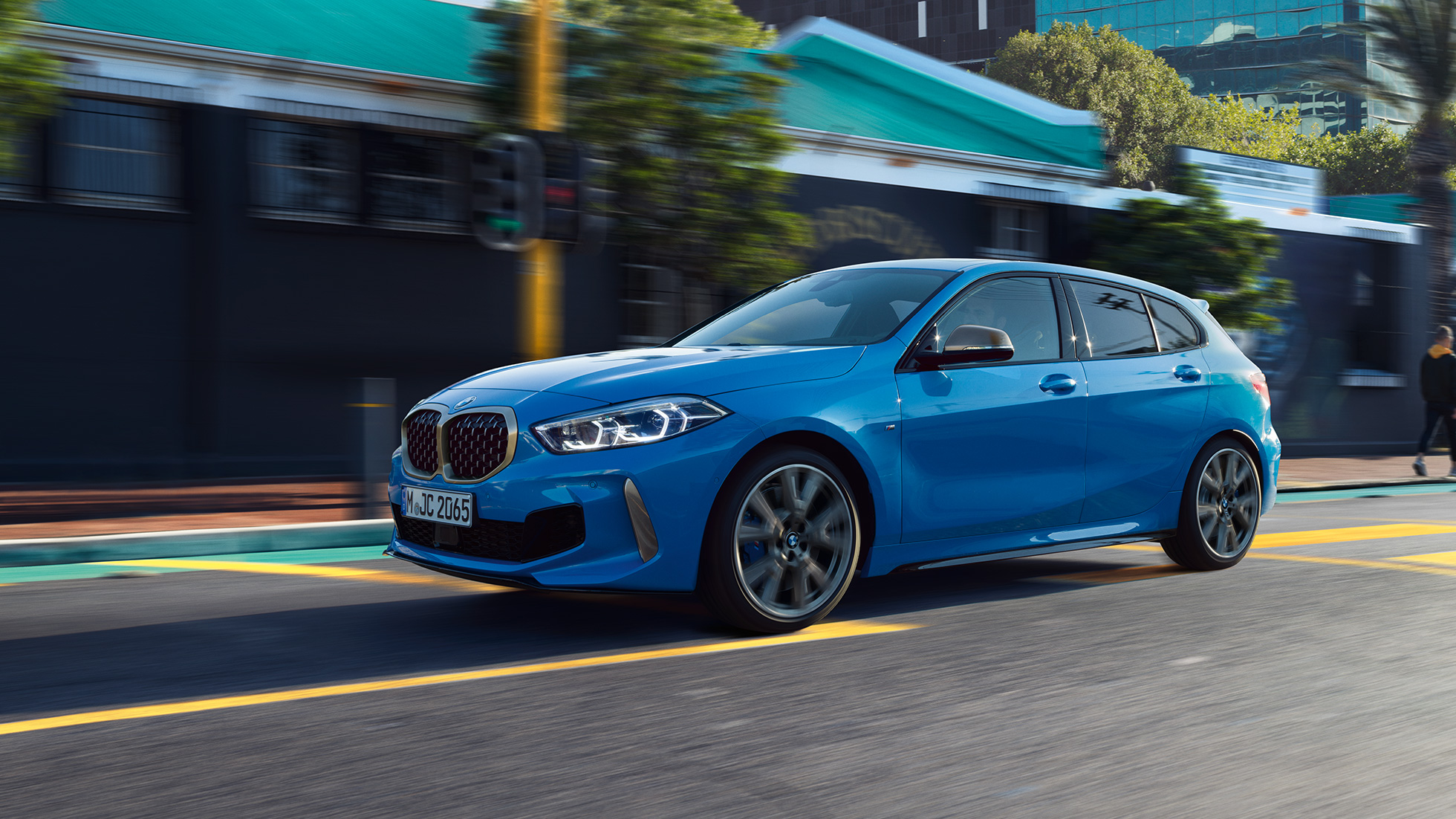 BMW Série 1, perspetiva lateral a três quartos. BMW Série 1 na pintura azul Misano metalizada, perspetiva frontal a três quartos do automóvel em movimento.