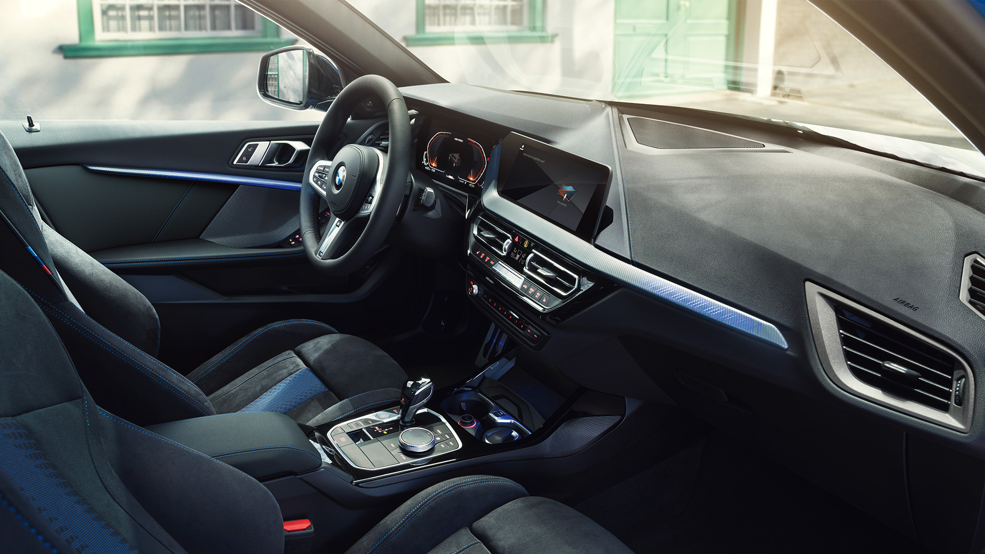 Interior desportivo do BMW Série 1. Posto de condução do BMW Série 1 com bancos desportivos M, volante M em pele e frisos interiores iluminados.