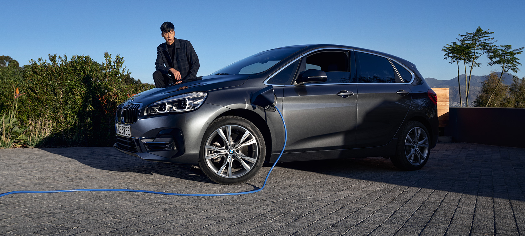 BMW 225xe Active Tourer híbrido plug-in, F45, perspetiva lateral a três quartos, a carregar BMW 225xe Active Tourer híbrido plug-in, F45, perspetiva lateral a três quartos, a carregar com um modelo