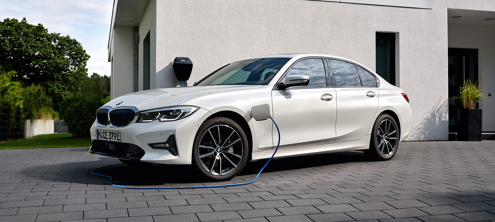 BMW Série 3 Berlina híbrido plug-in, 2021, G20, perspetiva lateral a três quartos, a carregar BMW Série 3 Berlina híbrido plug-in, 2021, G20, perspetiva lateral a três quartos, a carregar em frente a uma garagem