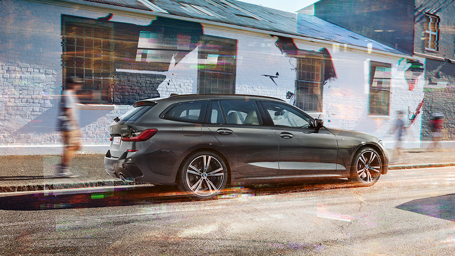 BMW Série 3 Touring (G21), pintura cinza Dravite, perspetiva traseira 7/8 BMW Série 3 Touring (G21), pintura cinza Dravite, perspetiva traseira 7/8, em movimento em frente a um edifício