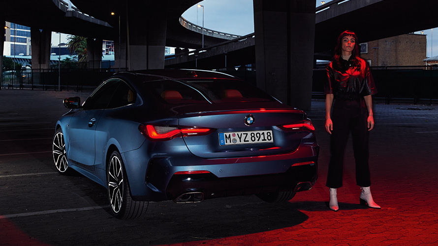 BMW Série 4 Coupé (G22), pintura azul Arctic Race metalizada, perspetiva traseira com uma pessoa BMW Série 4 Coupé (G22), pintura azul Arctic Race metalizada, perspetiva traseira com uma pessoa