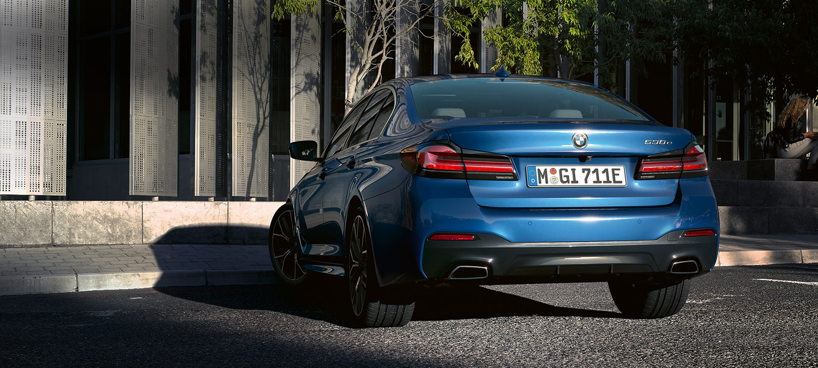 BMW Série 5 Berlina, eDrive (G30), azul Phytonic metalizada BMW Série 5 Berlina, eDrive (G30), azul Phytonic metalizada, perspetiva traseira, parado à frente de um edifício