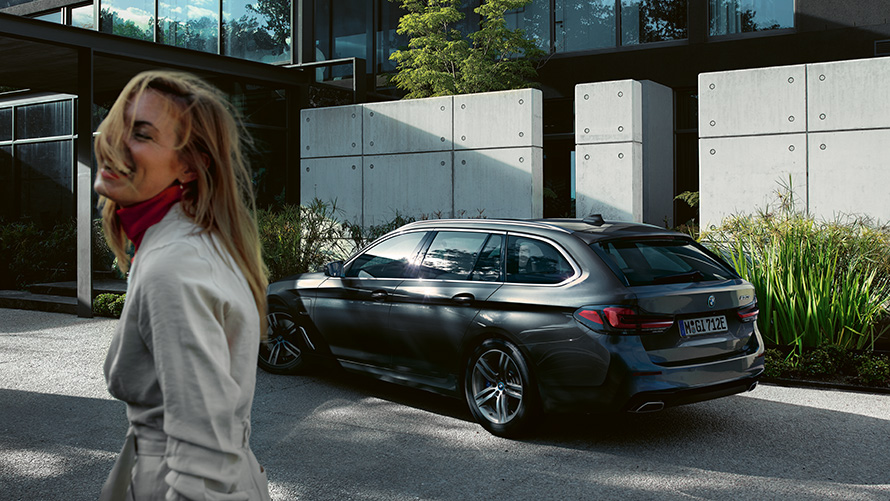 Mulher, BMW Série 5 Touring, G31, LCI, em cinza Sophisto com efeito brilhante metalizada, perspetiva lateral 7/8 Mulher à frente de um BMW Série 5 Touring parado, G31, atualização, 2020, em cinza Sophisto com efeito brilhante metalizada, perspetiva lateral 7/8
