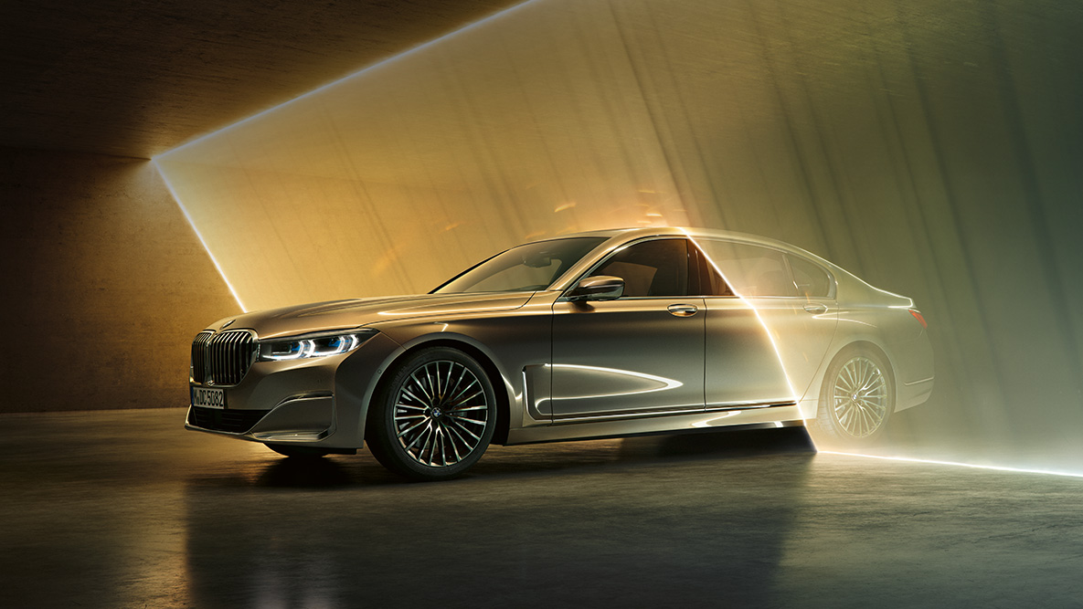 BMW Série 7 Berlina com perspetiva frontal a três quartos BMW Série 7 Berlina: BMW em cinza com perspetiva frontal a três quartos, rodeado por um feixe de luz
