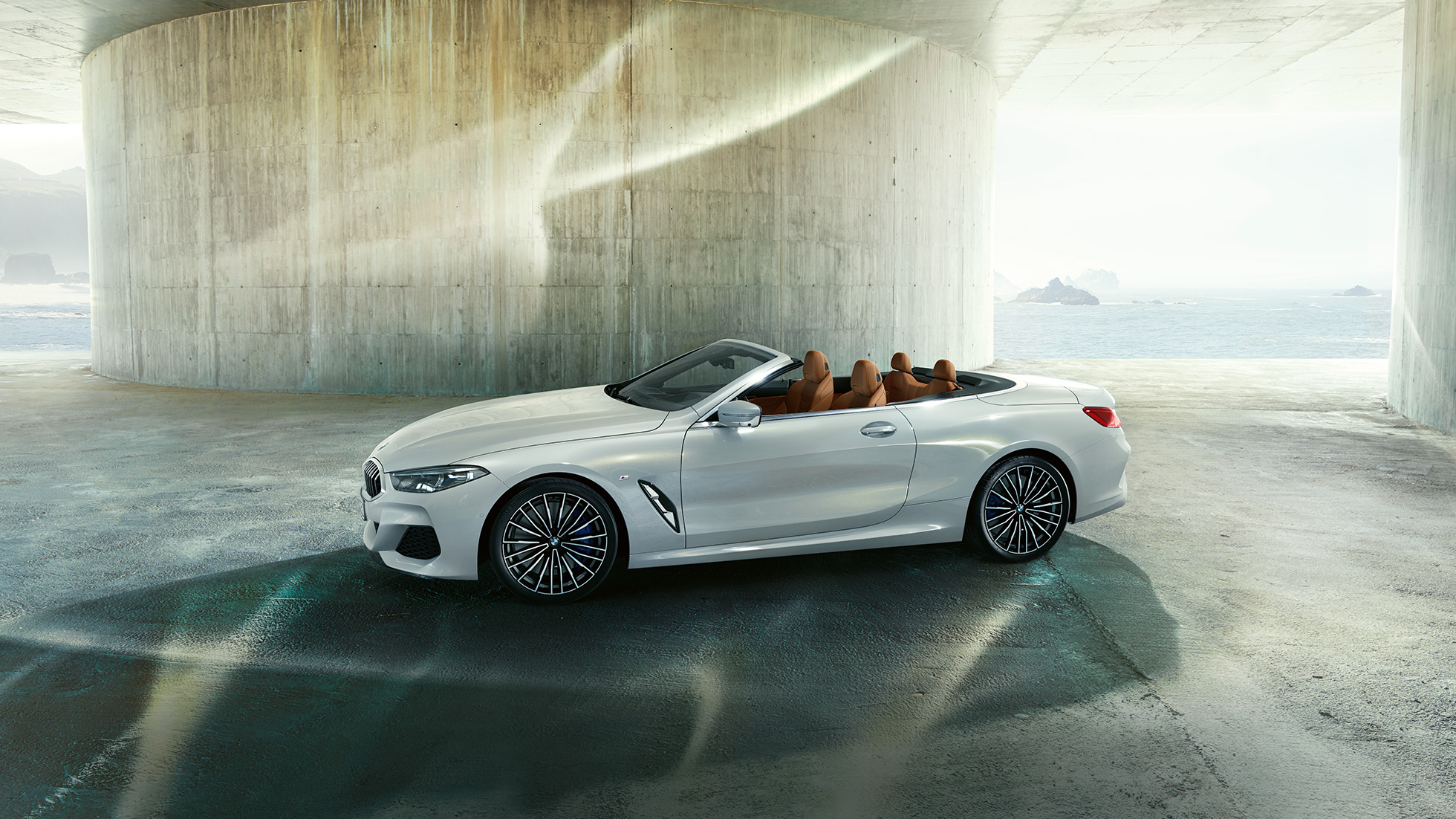 BMW M850i xDrive em branco Mineral metalizado, perspetiva lateral com capota flexível aberta. BMW M850i xDrive em branco Mineral metalizado, perspetiva lateral com capota flexível aberta.
