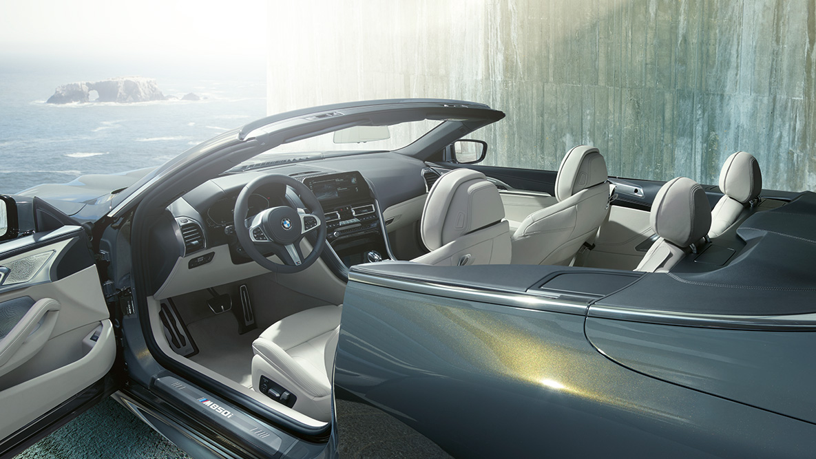 BMW M850i xDrive em cinza Dravit metalizado, interior, capota flexível e porta aberta. BMW M850i xDrive em cinza Dravit metalizado, interior, capota flexível e porta aberta.