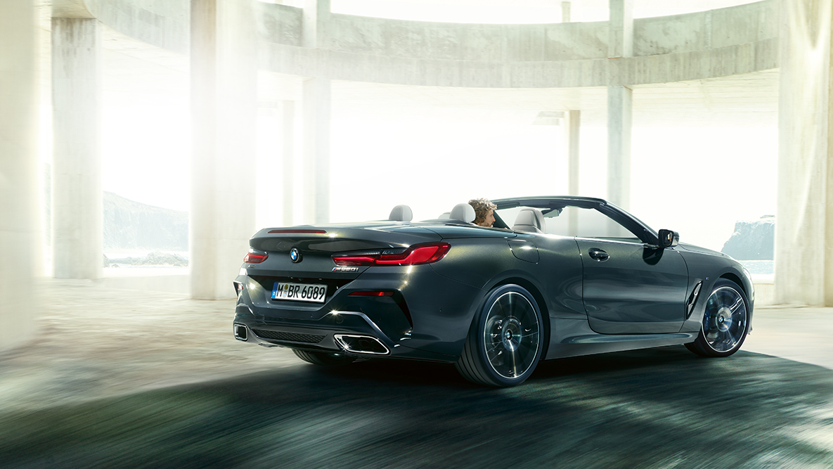 BMW M850i xDrive com capota flexível aberta, em movimento, perspetiva lateral. BMW M850i xDrive com capota flexível aberta, em movimento, perspetiva lateral.
