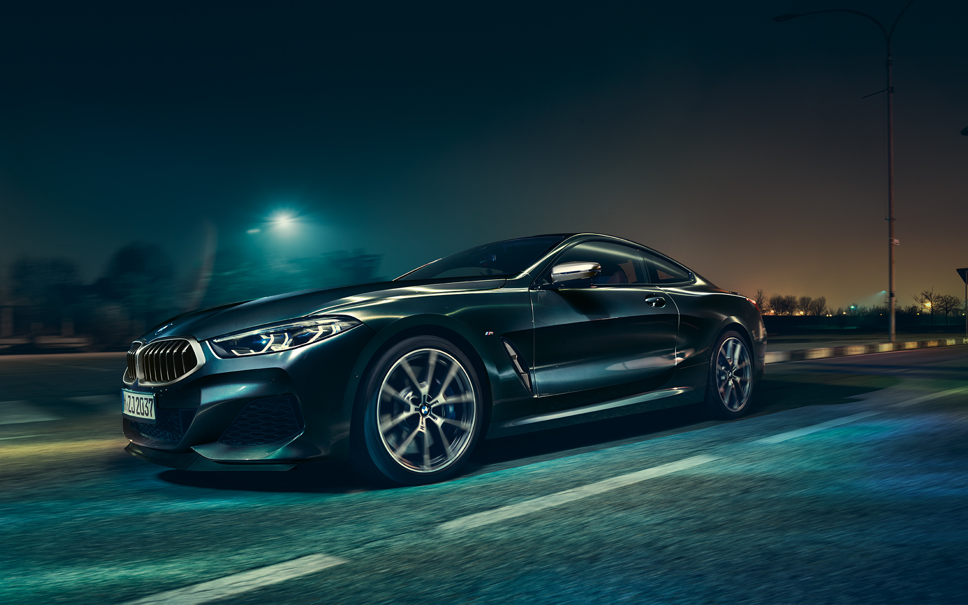 A three-quarter front still shot of the BMW 8 Series Coupé in an urban setting at night.