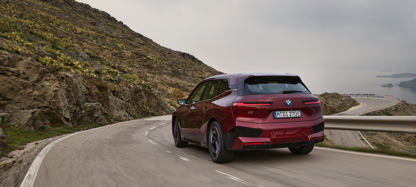 BMW iX, i20, 2021, SUV elétrico, BMW iX xDrive50, em movimento numa estrada costeira BMW iX, i20, 2021, SUV elétrico, BMW iX xDrive50, pintura vermelho Aventurin, perspetiva traseira, em movimento numa estrada costeira