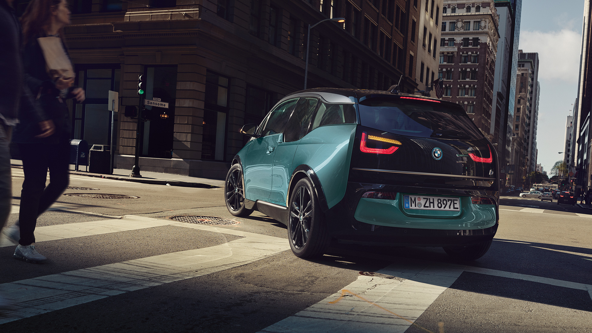 BMW i3 2018 em movimento, perspetiva traseira a três quartos BMW i3 I01 2018 bege Jucaro com realce em cinza Frozen metalizado em movimento num cenário urbano, perspetiva traseira a três quartos