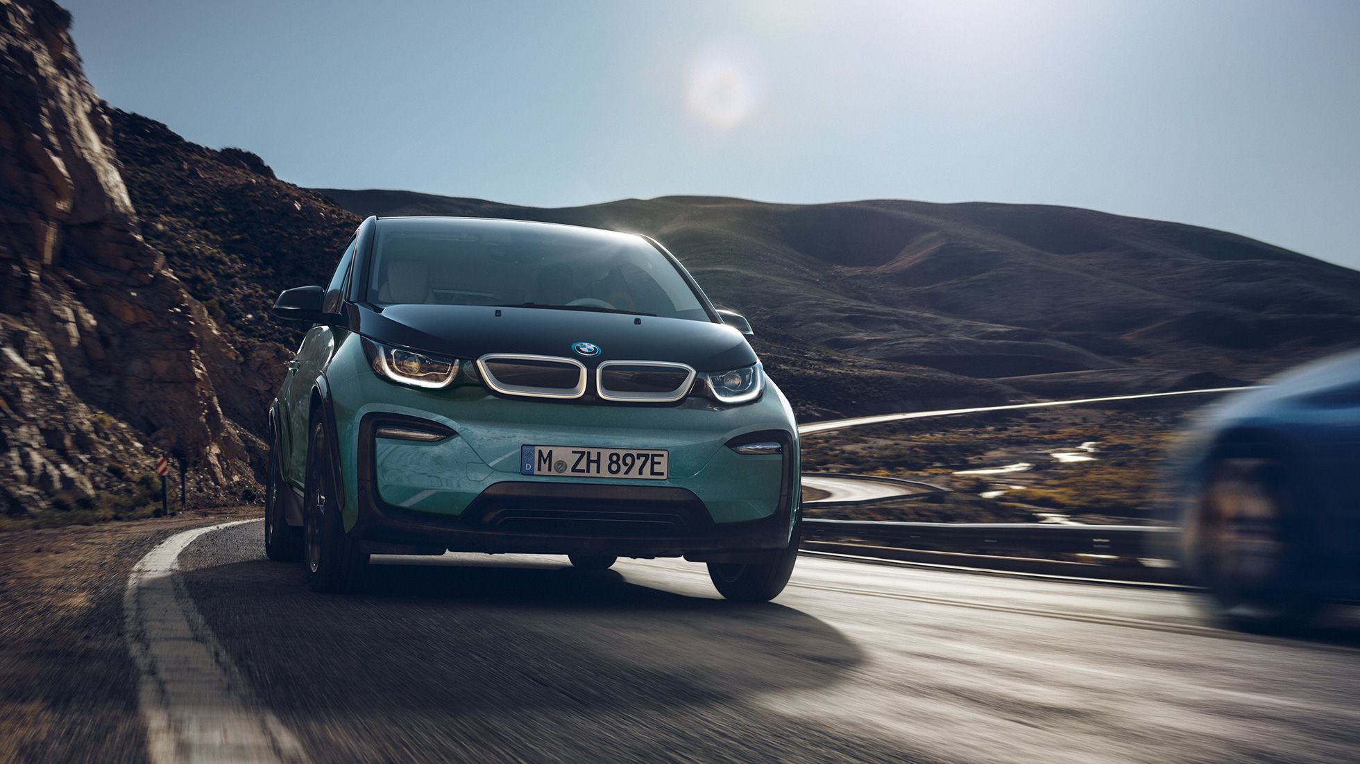 BMW i3 2018 em movimento, perspetiva lateral BMW i3 I01 2018 bege Jucaro com realce em cinza Frozen metalizado em movimento num cenário urbano, perspetiva lateral
