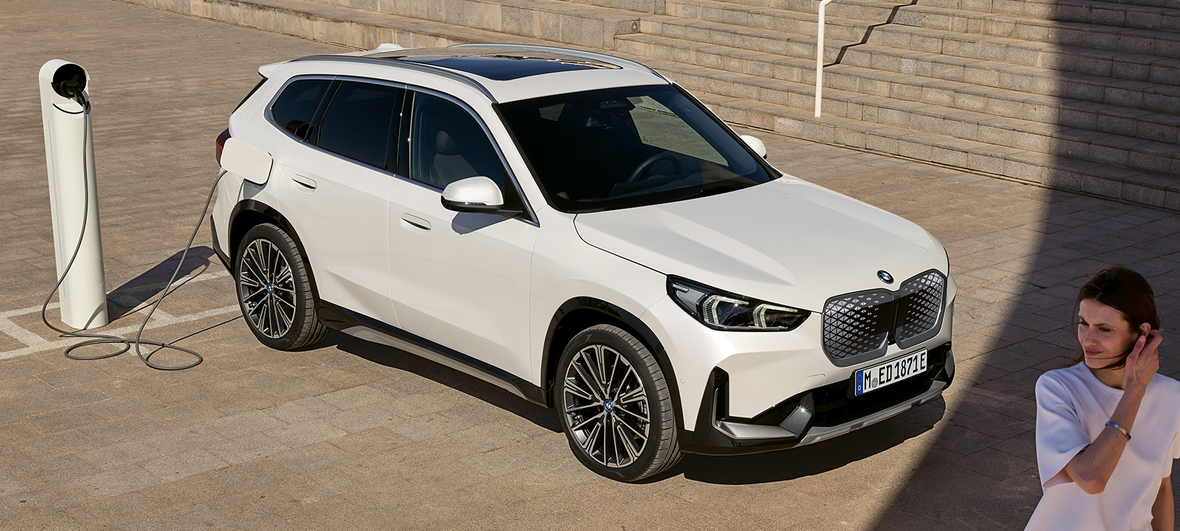 BMW iX1, U11, BEV, perspetiva lateral, a carregar BMW iX1, U11, BEV, 2022, pintura branco Mineral metalizada, perspetiva lateral a dois terços, a carregar, escadas