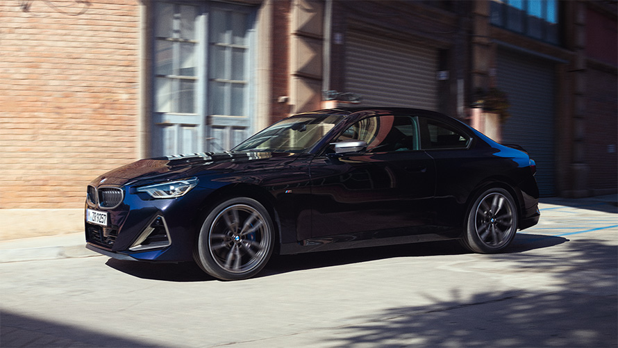 BMW M240i xDrive, G42, 2021, pintura preto Sapphire metalizada, perspetiva lateral a três quartos, parado em frente a um armazém