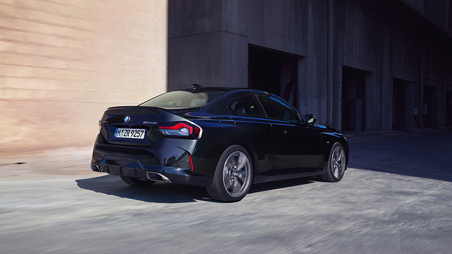 BMW M240i xDrive, G42, 2021, pintura preto Sapphire metalizada, perspetiva traseira a três quartos, parado em frente a um armazém