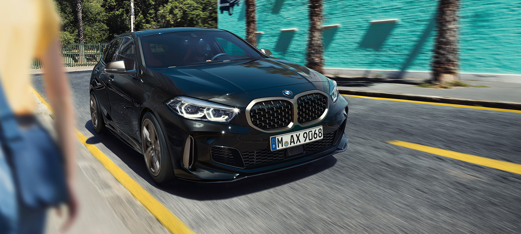 BMW M135i xDrive, perspetiva frontal a três quartos. BMW M135i xDrive na pintura preto Sapphire metalizada, em movimento, perspetiva frontal a três quartos.