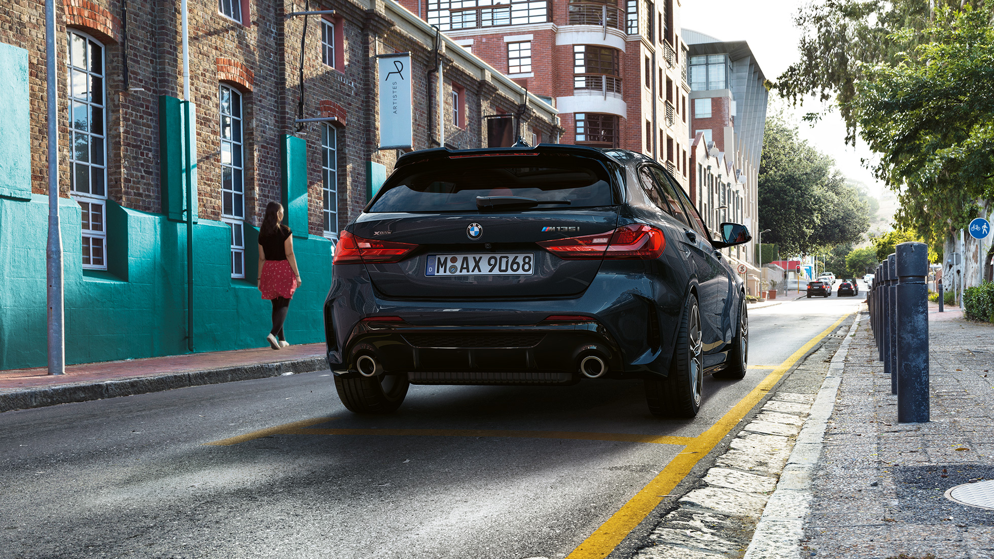 BMW M135i xDrive, perspetiva traseira. BMW M135i xDrive na pintura preto Sapphire metalizada, a estacionar, perspetiva traseira.