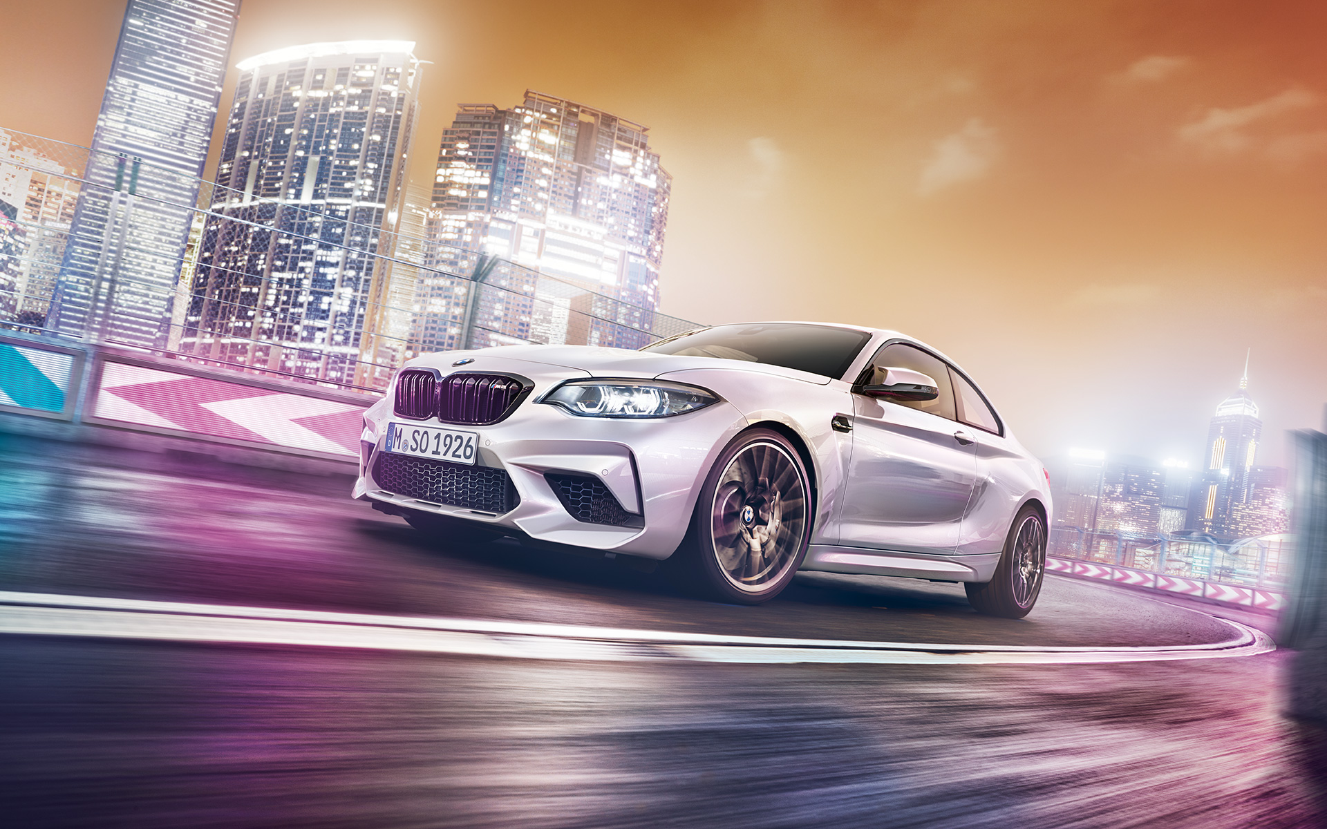 BMW M2 Competition em branco com paisagem de arranha-céus Um BMW M2 Competition branco em pista, frente a uma paisagem noturna com arranha-céus.