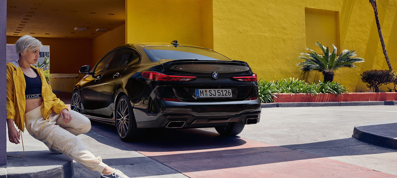 BMW M235i xDrive Gran Coupé, perspetiva traseira a três quartos BMW M235i xDrive Gran Coupé, pintura preto Sapphire metalizada, F44, perspetiva traseira a três quartos com mulher em frente