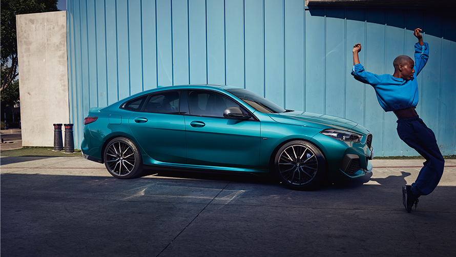 BMW M235i xDrive Gran Coupé, F44, perspetiva lateral com mulher à frente BMW M235i xDrive Gran Coupé, F44, pintura azul Snapper Rocks metalizada, perspetiva lateral com mulher à frente