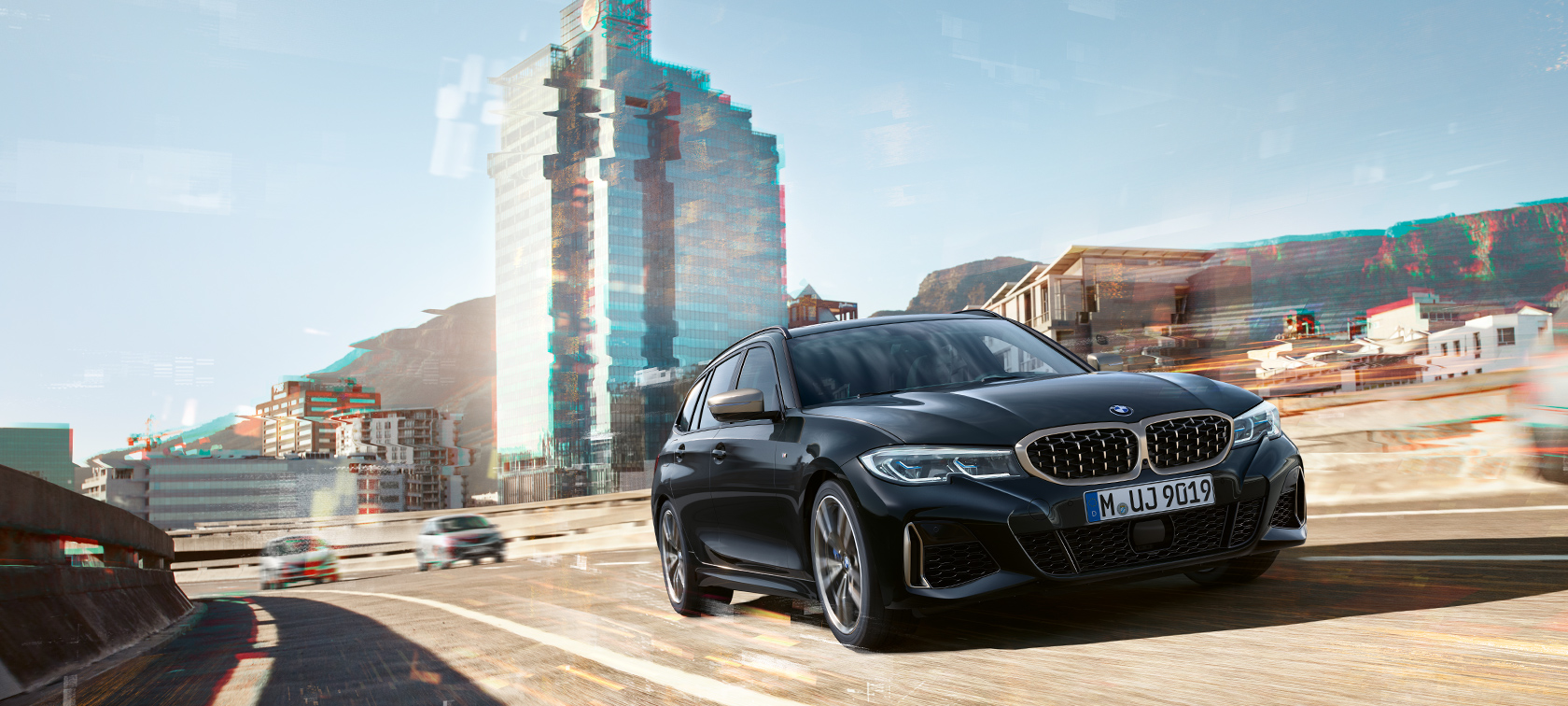 Perspetiva frontal a três quartos, em movimento, em frente a um cenário urbano BMW M340i xDrive Touring, perspetiva frontal a três quartos, em movimento, em frente a um cenário urbano