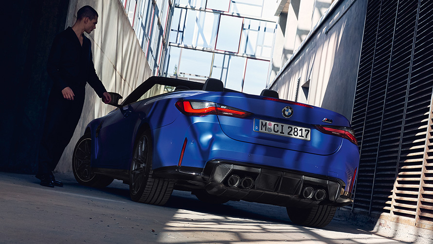 BMW M4 Competition Cabrio com M xDrive, G83, 2021, perspetiva traseira a três quartos BMW M4 Competition Cabrio com M xDrive, G83, 2021, pintura azul Frozen Portimao metalizada, perspetiva traseira a três quartos, com um homem
